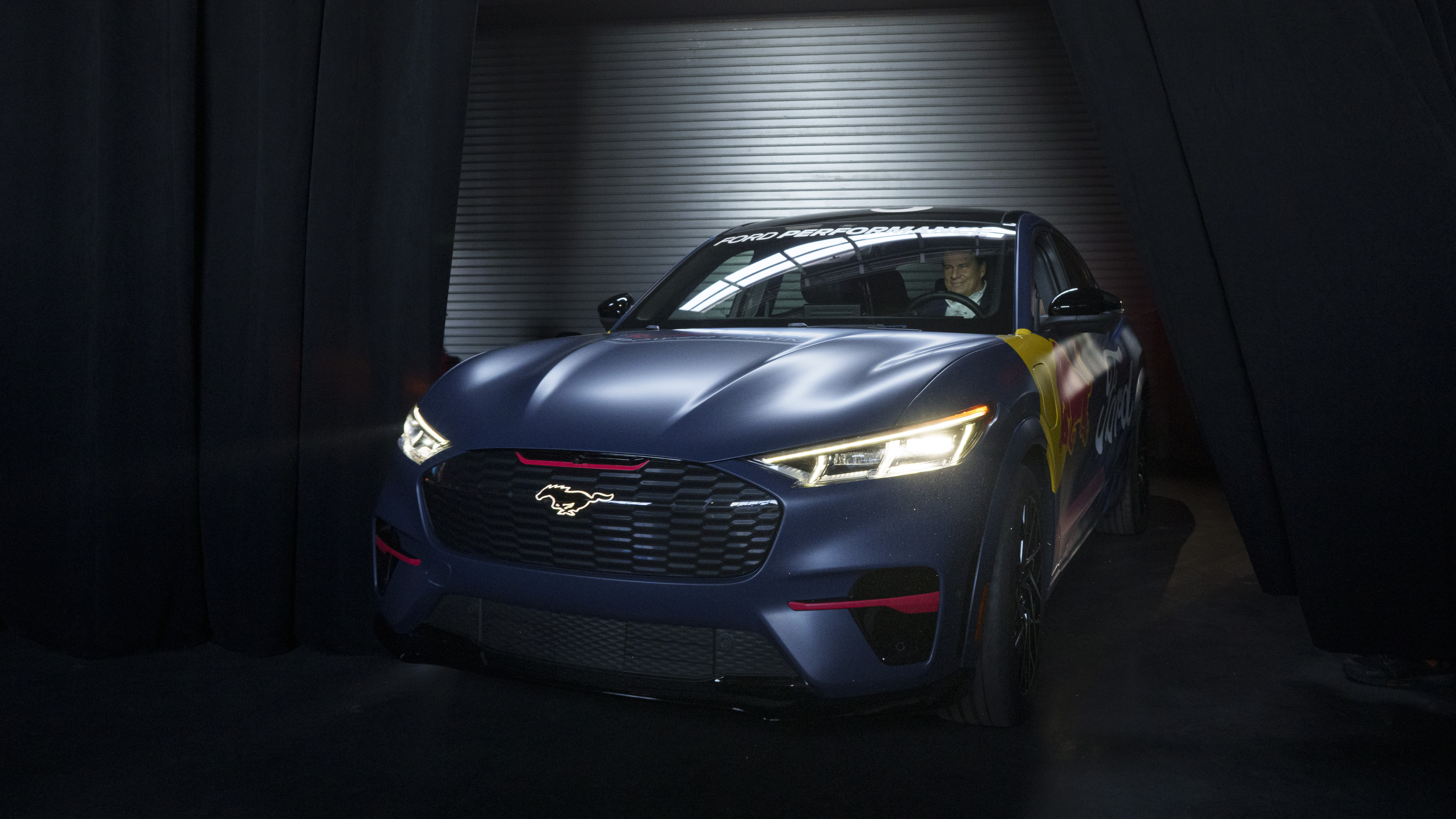 A blue and red Mustang in a dark room lit by one light above it